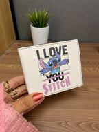 White wallet with 'I Love You Stitch' design held by a hand on a wooden surface.