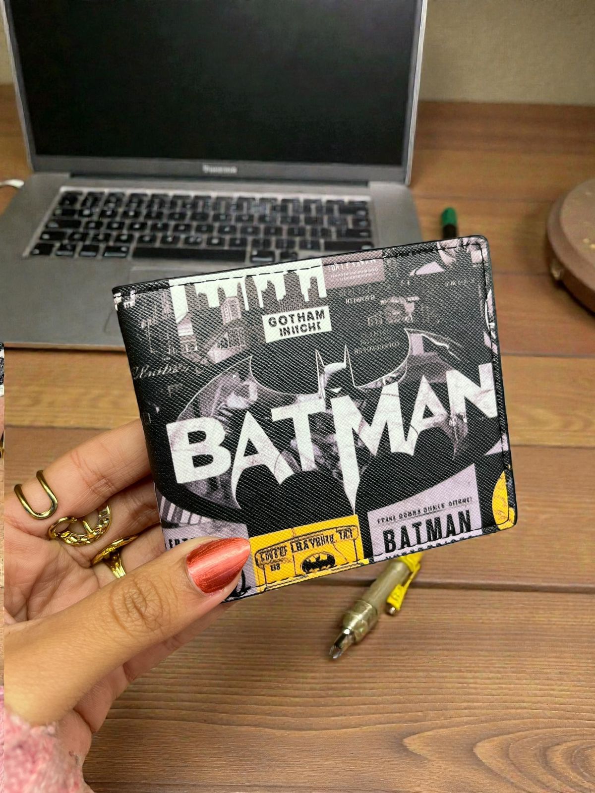 Batman wallet held by a hand with a laptop in the background