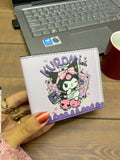 White wallet with cartoon character design held by a hand on a wooden surface with a laptop and mug in the background.
