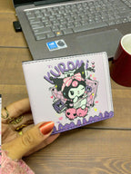 White wallet with cartoon character design held by a hand on a wooden surface with a laptop and mug in the background.